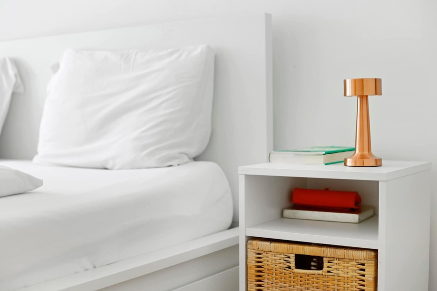 Cozy Bedside Nook With Soft Lighting.
Simple, Intentional Decor featuring a Woven Basket, Warm Copper Lamp, and your Favourite Reads within reach.